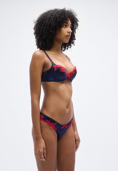 Granatowy zestaw bielizny z czerwonymi koronkowymi akcentami. Biustonosz z fiszbinami i kokardką; dopasowane majtki o kroju bikini z koronkową lamówką.