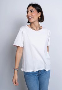 T-shirt di cotone bianco con maniche corte, con rifiniture rosse all'collo e ai bordi delle maniche. Abbinato a jeans di denim blu.