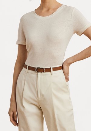 Femme portant un t-shirt beige ajusté à manches courtes, rentré dans un pantalon crème taille haute avec une ceinture marron.