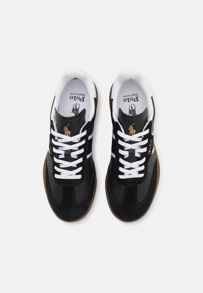 Zwarte en suède sneakers met witte veters en strepen, bruine rubberen zool, gouden logo-detail en zachte voering. Klassiek sportief ontwerp.
