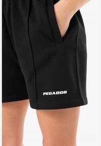 Černé bavlněné šortky se bočními kapsami, vyrobené z měkkého materiálu a s elastickým pasem. Na lemu je potisk "PEGADOR" bílou barvou.