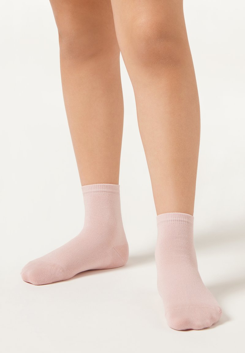 Lys lyserøde bomuldsstrømper med ribbede manchetter og en glat tekstur, hvilende på en lys baggrund.