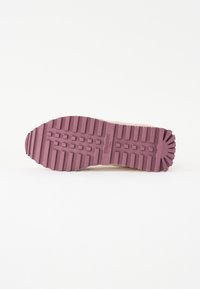 Semelle d'une basket avec un fond en caoutchouc texturé de couleur violette sombre, comportant des rainures parallèles et un logo en relief au centre.