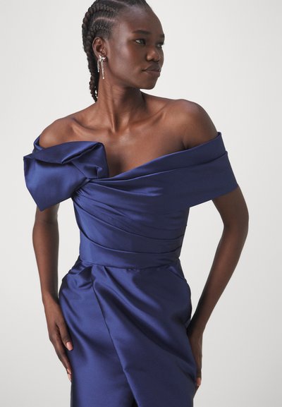 Navy satin dress with off-the-shoulder design, featuring a large bow on the left shoulder and draped detailing on the bodice and skirt.