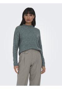 Pull en jersey ribbed bleu clair avec un col rond et des manches longues, associé à un pantalon gris ajusté avec des passants de ceinture et un détail de bouton.