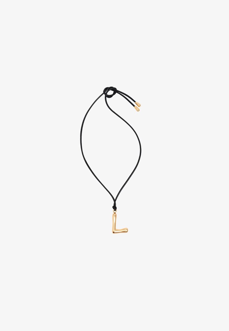Zelta tonī L burta piekariņš uz melnas virves kaklarotas, ar gludu tekstūru un regulējamiem slīdošajiem mezgliem garuma maiņai.