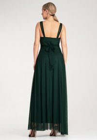 Długa zielona sukienka z szerokimi ramiączkami, dopasowanym górnym partem i zwiewnym dołem z przezroczystą warstwą oraz kokardą z tyłu.