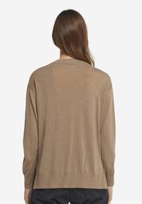 Brun stickad tröja med avslappnad passform, rund halsringning och långa ärmar; har ribbad nederkant och ärmslut för en strukturerad finish.