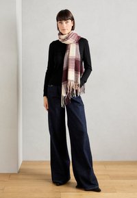 Mørkeblå vide jeans, svart langermet topp og et mønstret skjerf i krem, burgunder og grått med frynser.
