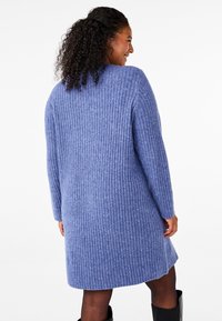 Vestido de punto acanalado en azul claro, con mangas largas, escote redondo y un corte holgado, que presenta una textura suave y una longitud a mitad del muslo.