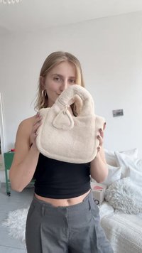 Beige fuzzy handbag with a curved handle, featuring a triangular accent, soft texture, and a rounded shape.