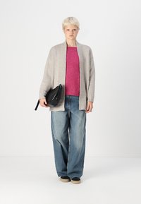 Grå strikket cardigan over en rosa teksturert genser, kombinert med vide blå jeans. En svart clutch-veske holdes i den ene hånden.