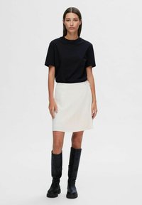 Czarny bawełniany t-shirt, biały spódnica w stylu wrap, czarne skórzane buty do kolan. Minimalistyczny design, jednolite kolory i czyste linie przez cały czas.