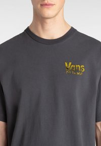 Gray cotton t-shirt with short sleeves, featuring a yellow Vans logo on the left chest area in a textured, distressed font.