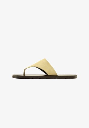 Beige Wildleder-Zehensandale mit breitem Riemen über dem Fuß und flacher dunkelbrauner Sohle, von der Seite betrachtet.