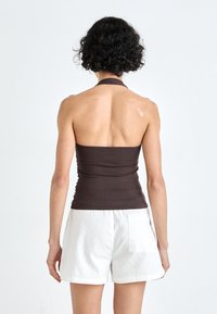 Brown fitted halter top with ruched texture, paired with white shorts featuring a back pocket. Minimalist design against a light background.