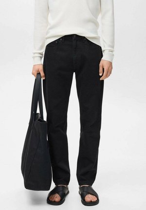 Black denim jeans with a straight-leg fit, worn with a white ribbed top and black sandals, held a black tote bag. Simple design, no visible patterns.