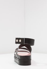 Černá kožená sandál s tlustou podešví, zapínáním na kotníku a stříbrnými knoflíky. Hladký povrch s růžovou stélkou a minimalistickým designem.