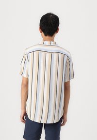 Chemise à manches courtes avec des rayures verticales bleu clair, beige et noires ; tissu doux avec un col boutonné et un ourlet arrondi.