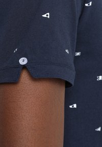 Chemise à manches courtes bleu marine en coton, avec de petits motifs géométriques blancs et un détail boutonné à l'ourlet des manches.