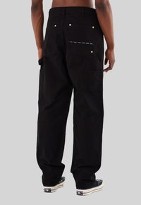 Pantaloni cargo neri con una vestibilità ampia, dotati di due tasche posteriori e una striscia decorativa su una tasca. Realizzati in tessuto resistente.