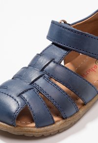Námořnické modré kožené sandály s křížovým designem, otevřenou špičkou a nastavitelným popruhem. Obsahují prošívané detaily a strukturovanou gumovou podrážku.