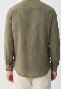 Olivově zelená košile s dlouhým rukávem, rovný spodní lem a manžety na knoflíky. Vyrobena z texturované látky, pohled zezadu ukazuje hladký povrch.