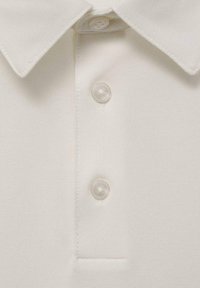 White polo shirt made of textured fabric with a collar, three transparent buttons, and a stitched neckline.