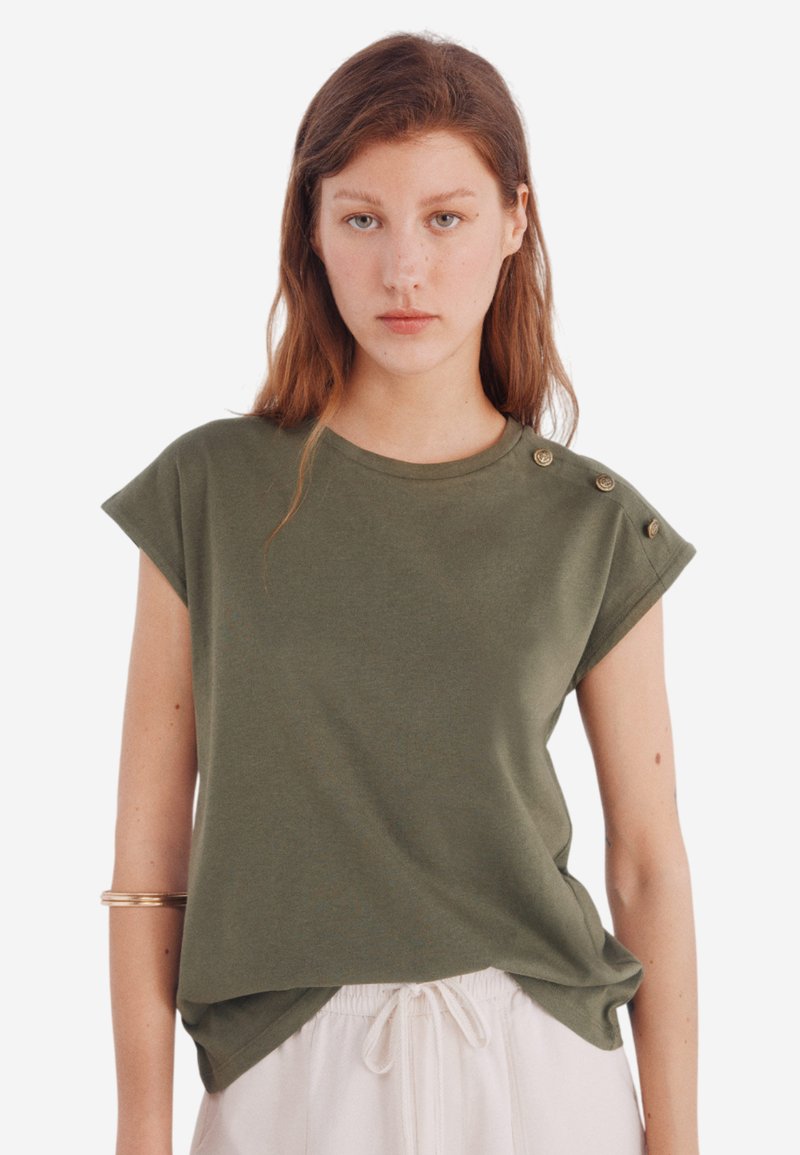 Oliven grøn kortærmet t-shirt med rund hals, dekoreret med knapper på skulderen og en afslappet pasform, lavet af blødt stof.