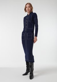 Conjunto de dos piezas de punto en azul marino que incluye una chaqueta corta con cierre de botones y una falda a juego, ambos adornados con costuras blancas y bolsillos.