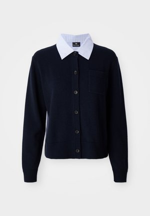 Cardigan blu navy con chiusura a bottoni, polsini a coste e una tasca. Presenta una camicia colletto a strisce bianche e blu sotto.