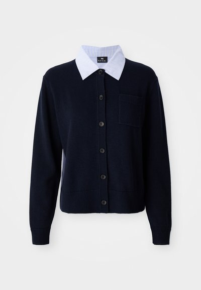 Cardigan blu navy con chiusura a bottoni, polsini a coste e una tasca. Presenta una camicia colletto a strisce bianche e blu sotto.