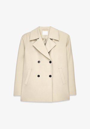 Bēšas divrindas mētelis ar plašu apkakli, melnām pogām un sānu kabatām. Gluda tekstūra, pielāgota piegriezuma forma, nav redzamu rakstu.