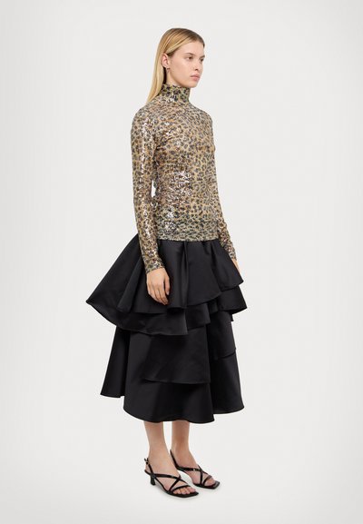 Haut à manches longues en sequins dorés avec un col haut, associé à une jupe en satin noire à plusieurs niveaux. Des sandales noires à brides complètent le look.