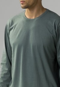 Koszula z długim rękawem w przytłumionym zielonym kolorze, wykonana z miękkiego materiału. Posiada okrągły dekolt i wytłoczone logo "ATLANTIC" na piersi. Prosty design.