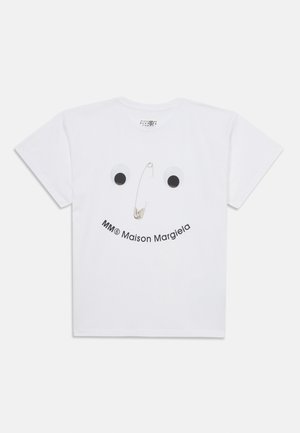 T-shirt bianco in cotone con un design di faccia giocosa con occhi mobili e un fermaglio di sicurezza. Testo che recita "MM® Maison Margiela" sotto la faccia.