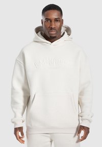 Sudadera de color beige claro con un bolsillo tipo canguro, diseño oversize, puños acanalados y logo bordado en el pecho. Fabricada con tela texturizada.