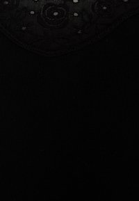 Black top featuring a floral lace neckline with circular cutouts, smooth texture, and ribbed fabric on the body.