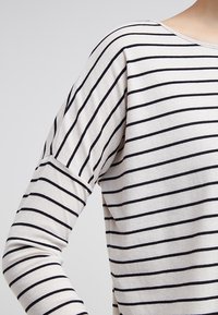 Gestreepte lange mouwen top in crème en marineblauw. Kenmerkt zich door lichte, zachte stof met horizontale strepen, ronde halslijn en licht gepofte schouders.