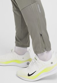 Harmaat urheiluhousut, joissa on sivuvetoketjut, yhdistettyinä valkoisiin ja neonkeltaisiin Nike-tennareihin, joissa on musta logo ja teksturoitu yläosa.