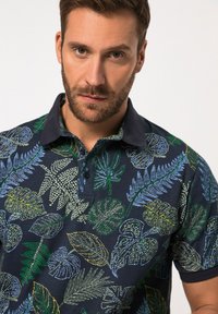 Polo shirt blu navy con un motivo di foglie colorato in verde, blu e giallo, con un colletto a contrasto nero e una pattina dei bottoni.