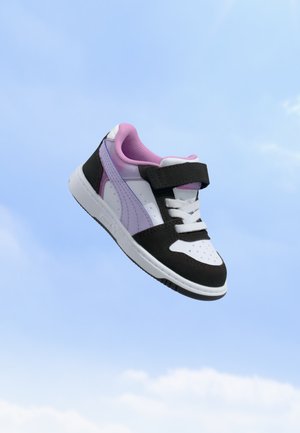 Baskets enfant en blanc, noir et violet clair avec une bride velcro et des lacets, flottant sur un fond de ciel bleu clair.