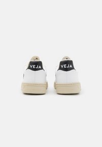 Sneaker bianche con tabelle nere sul tallone, con il nome del brand "VEJA" in bianco. Suole in gomma con una suola intermedia beige testurizzata, upper in pelle liscia.