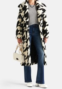 Płaszcz w czarno-białą pepitkę o pluszowej teksturze, szary dziergany top, niebieskie dzwonowate dżinsy, biała torebka i białe buty na platformie.
