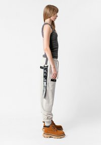 Top sin mangas gris, pantalones de chándal beige claro con parches negros y botines marrón claro. Los pantalones de chándal tienen detalles laterales y una cintura con cordón.