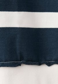 Tissu tricoté à rayures horizontales bleu marine et blanc avec un tissu côtelé blanc en dessous, montrant un bord légèrement effiloché.