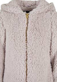 Luddig, ljusrosa zip-up jacka med huva, som har en gyllene dragkedja och textil med en tjock, mjuk utseende.