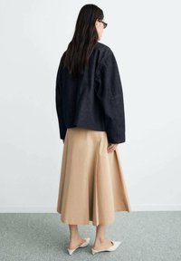 Dark denim oversized jacket, beige long skirt with pleats, white slip-on shoes, minimalistic design, textured fabric, back view.