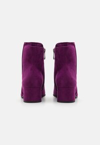 Purple suede ankle boots with block heels, featuring zip closures on the sides and a smooth texture.