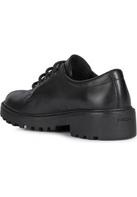 Scarpe nere in pelle con finitura liscia, punta rotonda, design con lacci e suola in gomma testurizzata con un piccolo logo sul tallone.